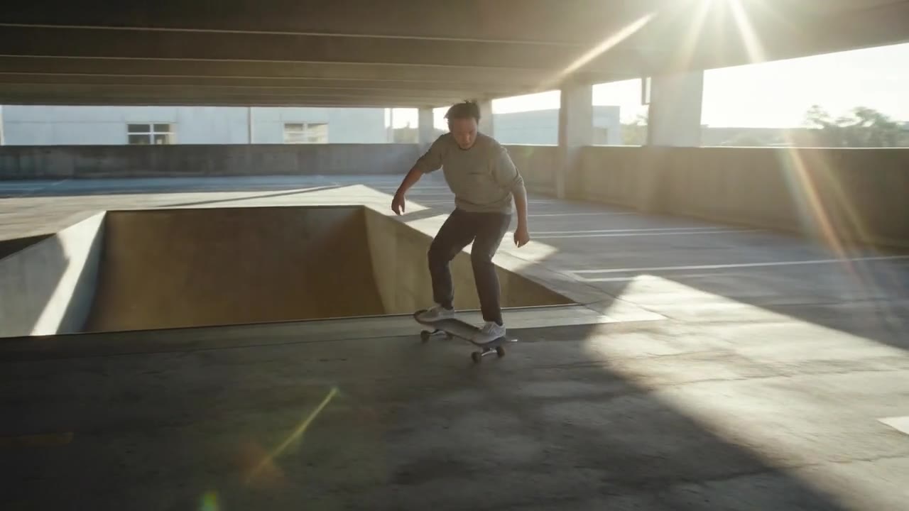 A skateboarder riding through a sunlit empty parking garage