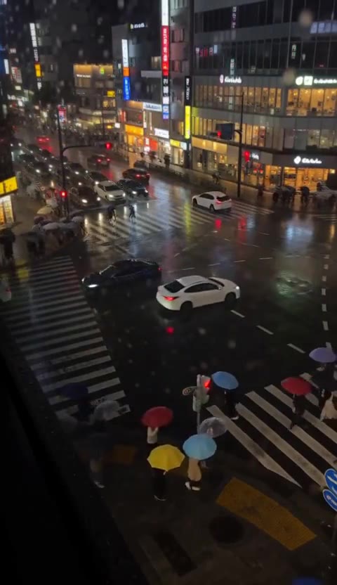 Colorful umbrellas crossing a wet city street at night, seen from above